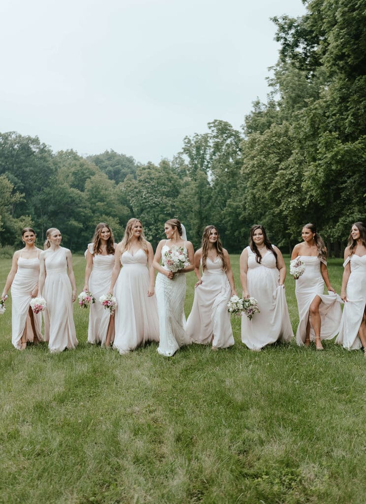 Bridesmaids wearing light pink dresses walk with bride through an open field