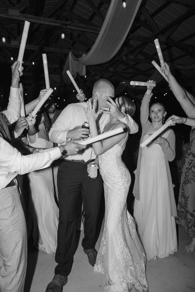 Bride and groom kiss on the dance floor while covering their faces with their hands, displaying their wedding rings