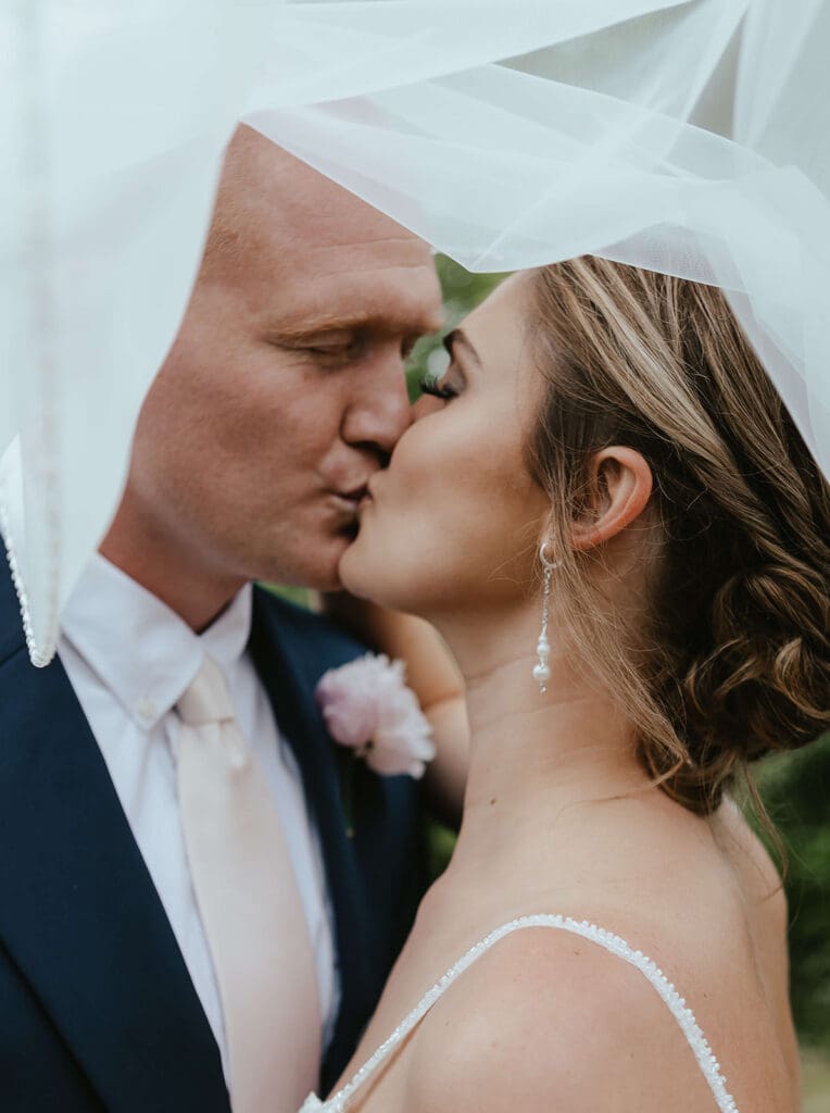 Bride and groom kiss underneath the bride's veil