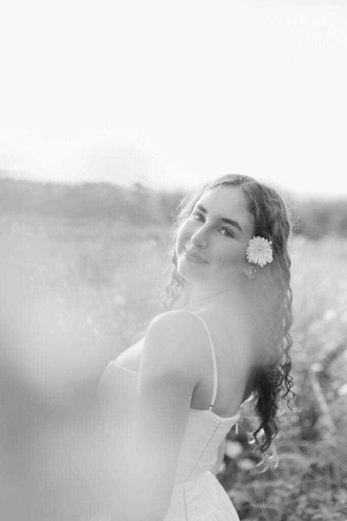 Senior in a field smiles and has a daisy tucked behind her ear