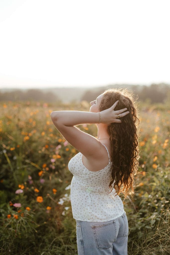 Girl holds her hair and closes her eyes in a field of wildflowers at sunset