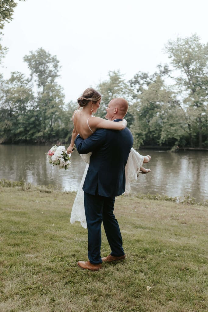 Groom carries bride outdoors with a creek in the background