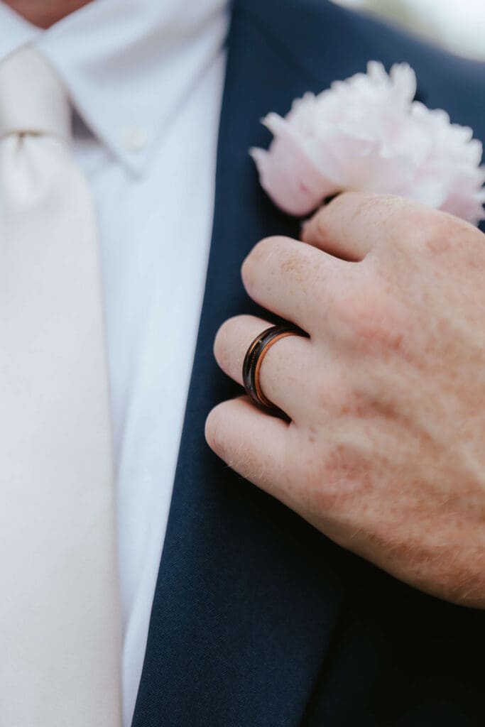 Close up image of groom wearing wedding ring and wearing a boutonniere