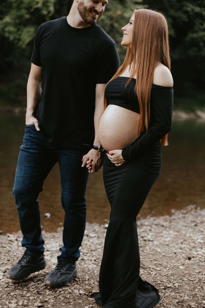 Couple gazes into each other's eyes during their maternity photos on the banks of a creek