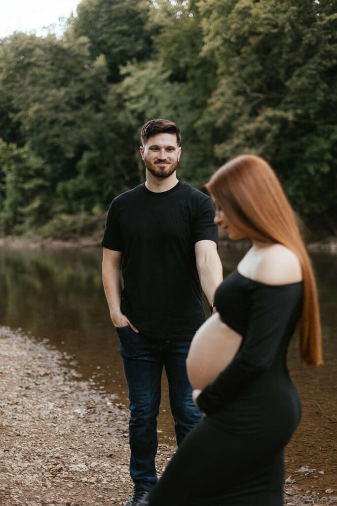 Man holds out hand to pregnant wife on the bank of a creek