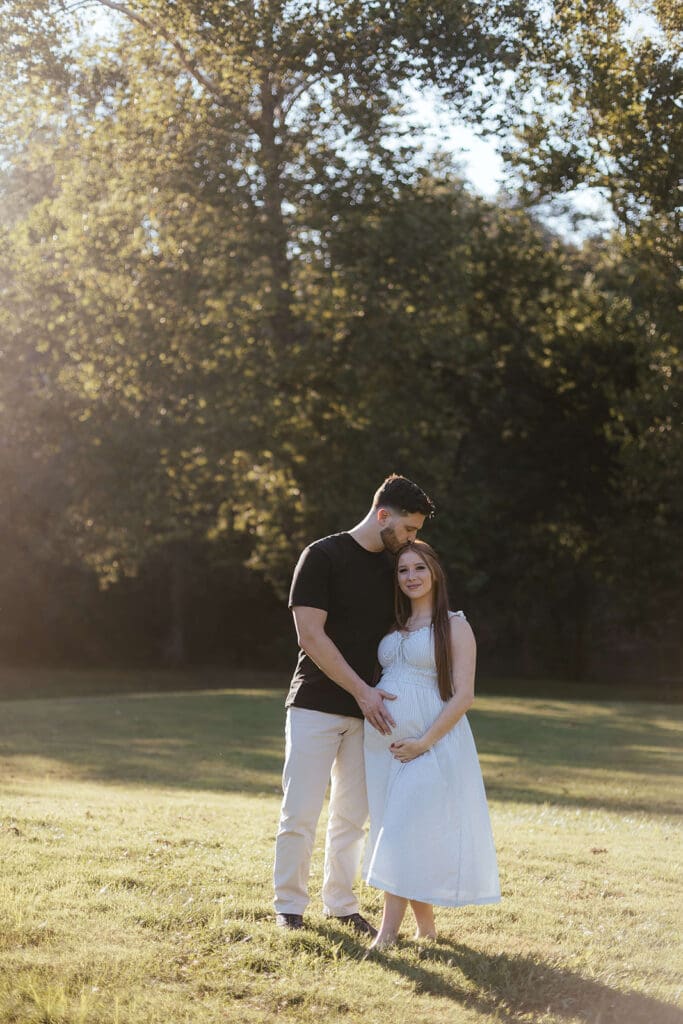 Man holds pregnant wife's stomach in a field in Lancaster County Central Park