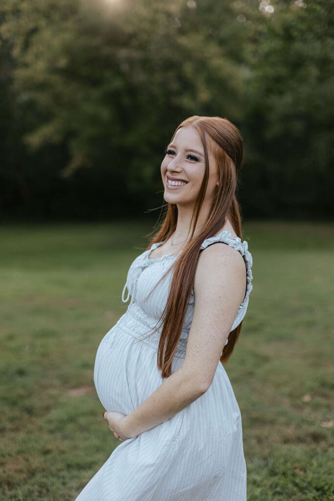 Woman hold belly and smiles during outdoor maternity photos at Lancaster County Central Park
