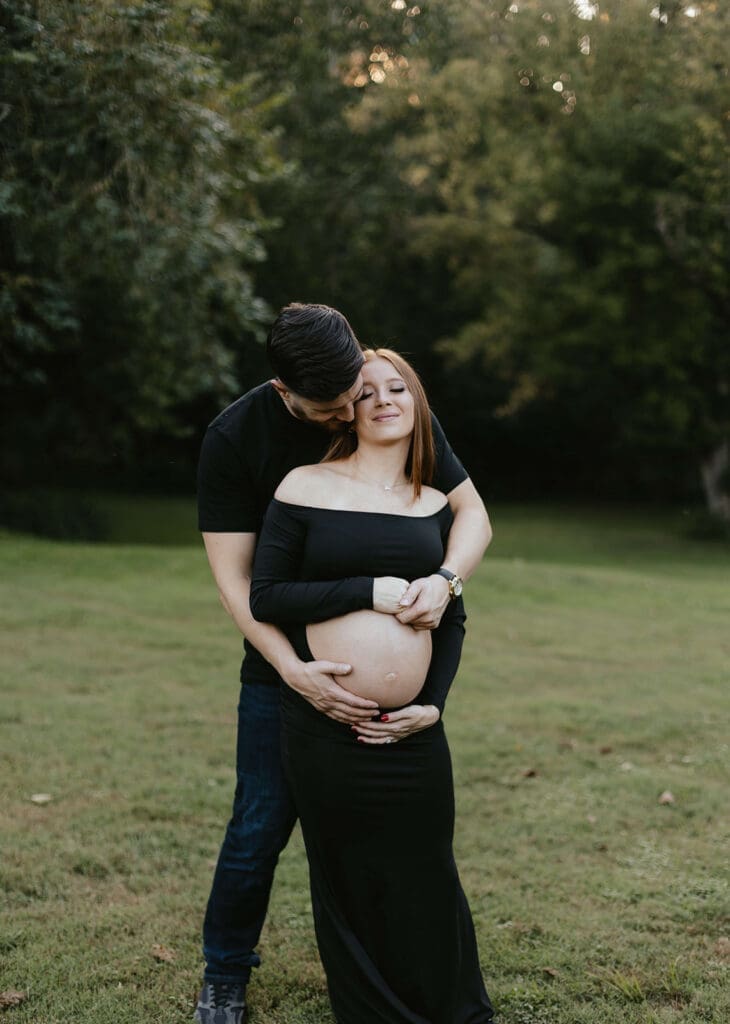 Man holds pregnant wife's stomach in a field in Lancaster County Central Park