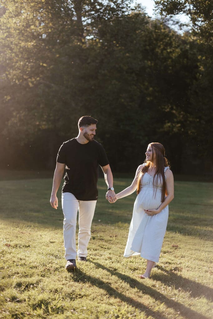 Man and pregnant woman hold hands and walk in a field during their outdoor maternity photos