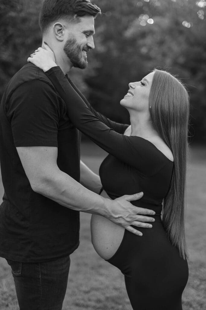 Man and woman embrace each other and smile at each other during their maternity photo shoot