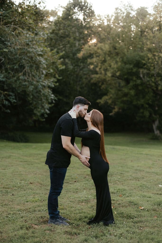 Man kisses woman and touches her belly while standing in a field in a park