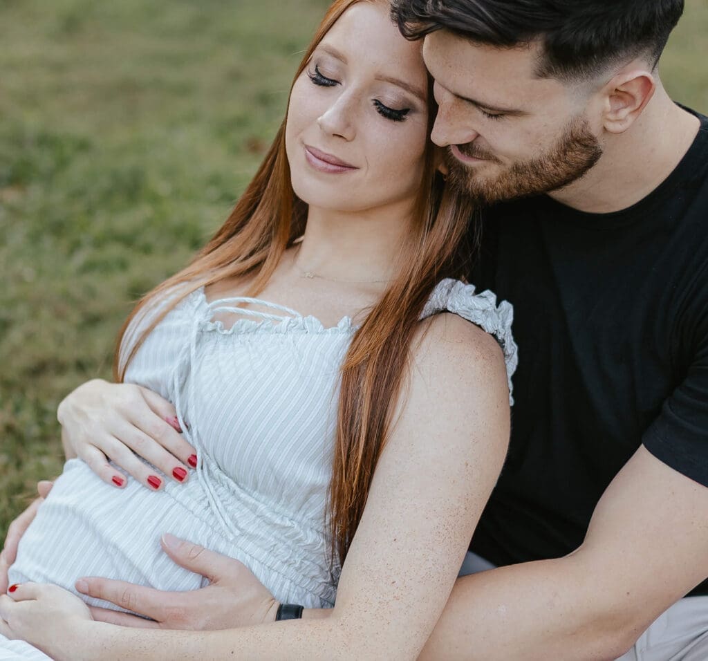 Man and pregnant woman sit together in a field and smile