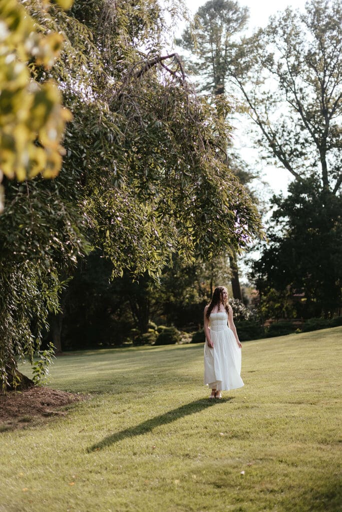 Senior in long, flowing white dress walks in an open field