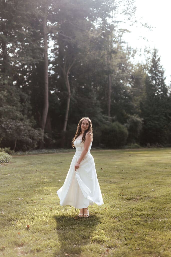 Senior in long, flowing white dress stands in an open field