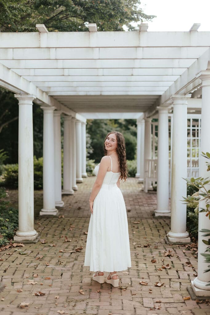 Portrait of senior in a long white dress, standing under a pergola