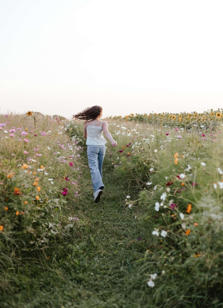 Girl runs through a field of wildflowers in the evening wearing a white tank top and jeans