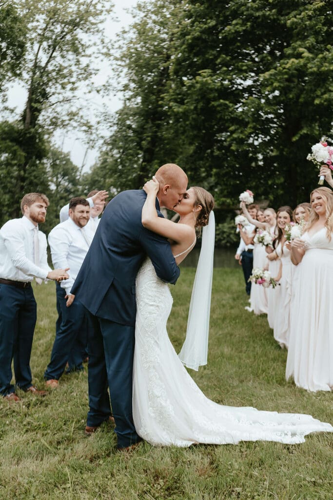 Bride and groom kiss while surrounded by groomsmen on one side and bridesmaids on another