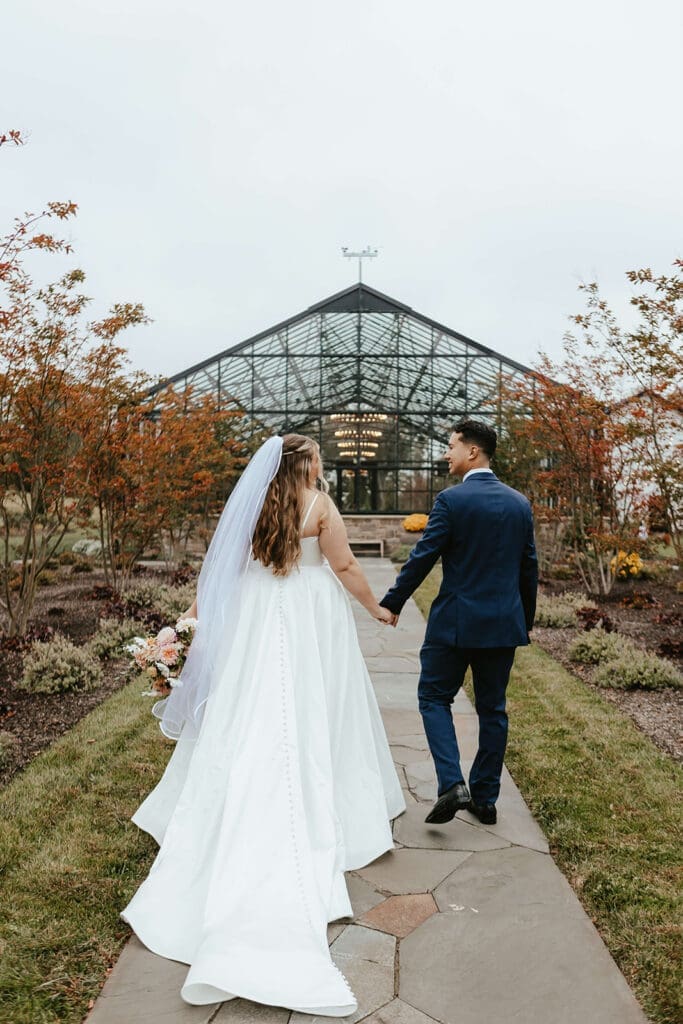 Bride and groom walk towards the greenhouse at Westwynd Gardens