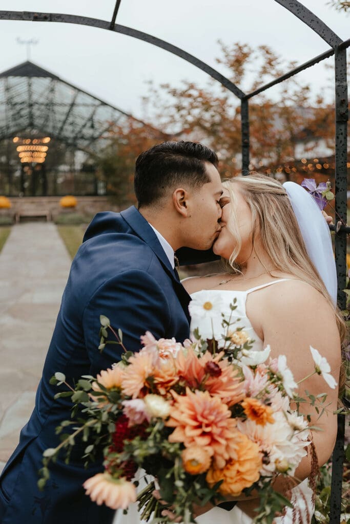 Bride and groom kissing outside Westwynd Gardens' greenhouse