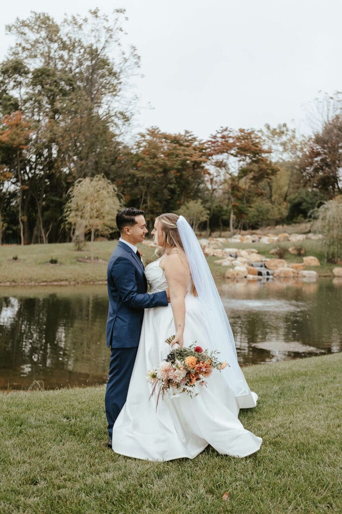 Bride and groom stare lovingly at each other by the pond at Westwynd Gardens