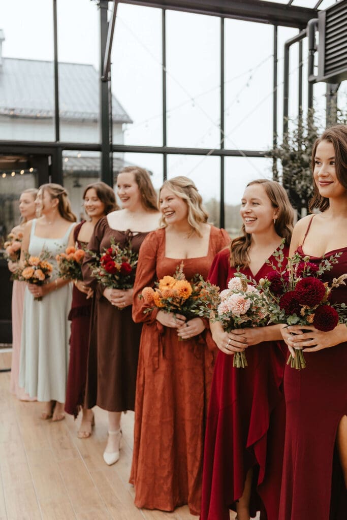 Bridesmaids smiling dressed in earthy fall colors like red, orange, and brown