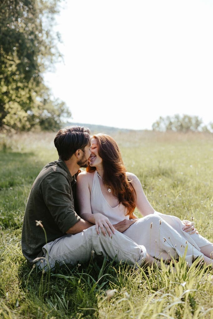 Couple kisses while sitting outdoors in a field in the Pennsylvania countryside