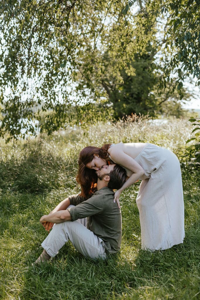 Woman kisses her fiancé in a field in the countryside during their summer engagement photos