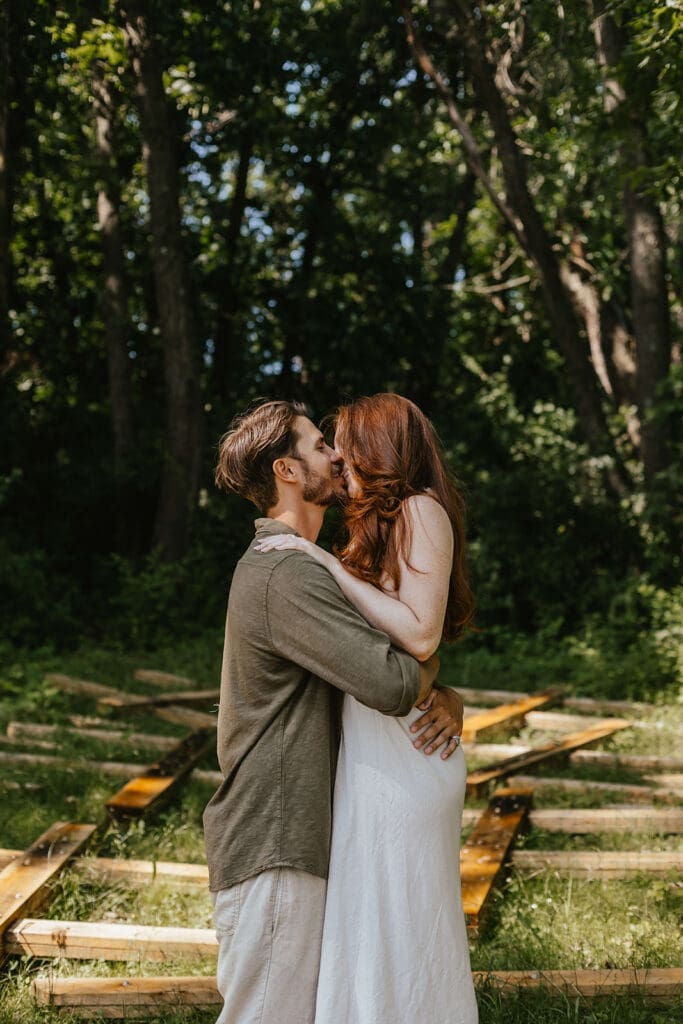 Romantic candid of a man and woman kissing in a clearing of trees