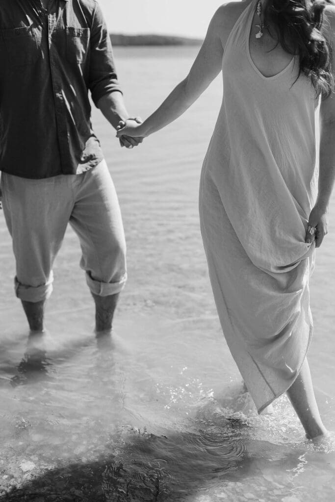 Candid photo of an engaged couple holding hands while walking barefoot through a lake