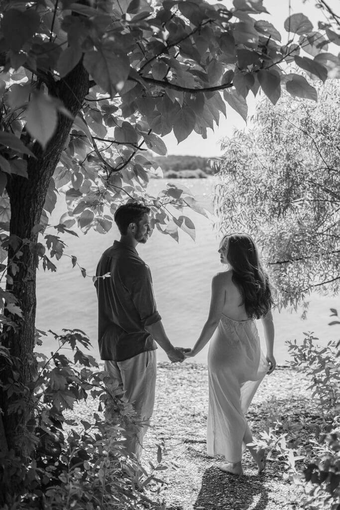 Candid photo of an engaged couple holding hands by a lake