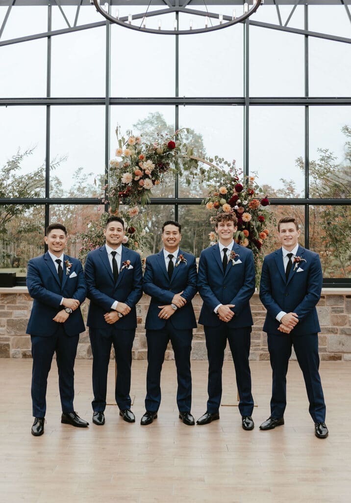 Groom with groomsmen wearing navy suits in a greenhouse