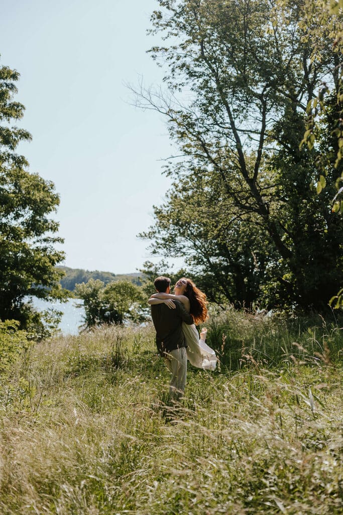 Romantic summer engagement photo of woman hugging her fiancé in the countryside