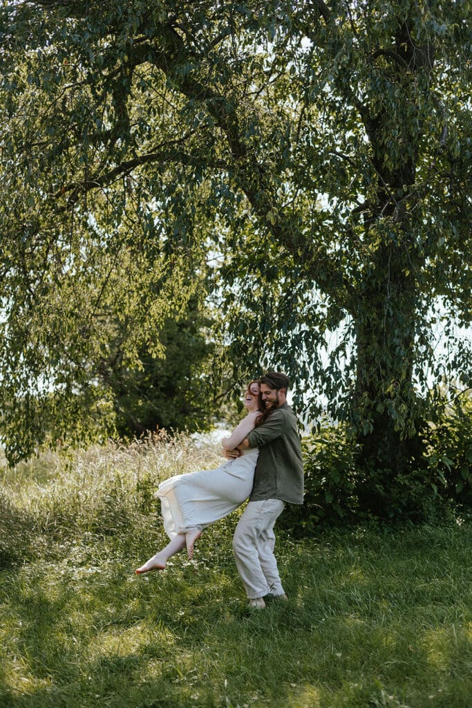Candid photo of woman laughing as her fiancé swings her in a field in the summer