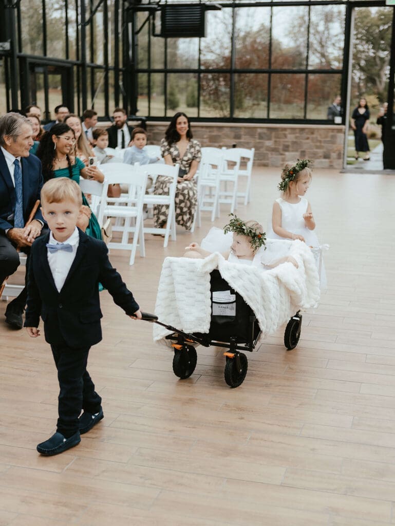 Ring bearer pulling the flower girl down the aisle in a wagon