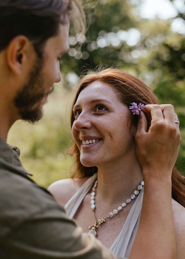 Up close shot of man tucking a flower behind his fiancée's ear as she smiles