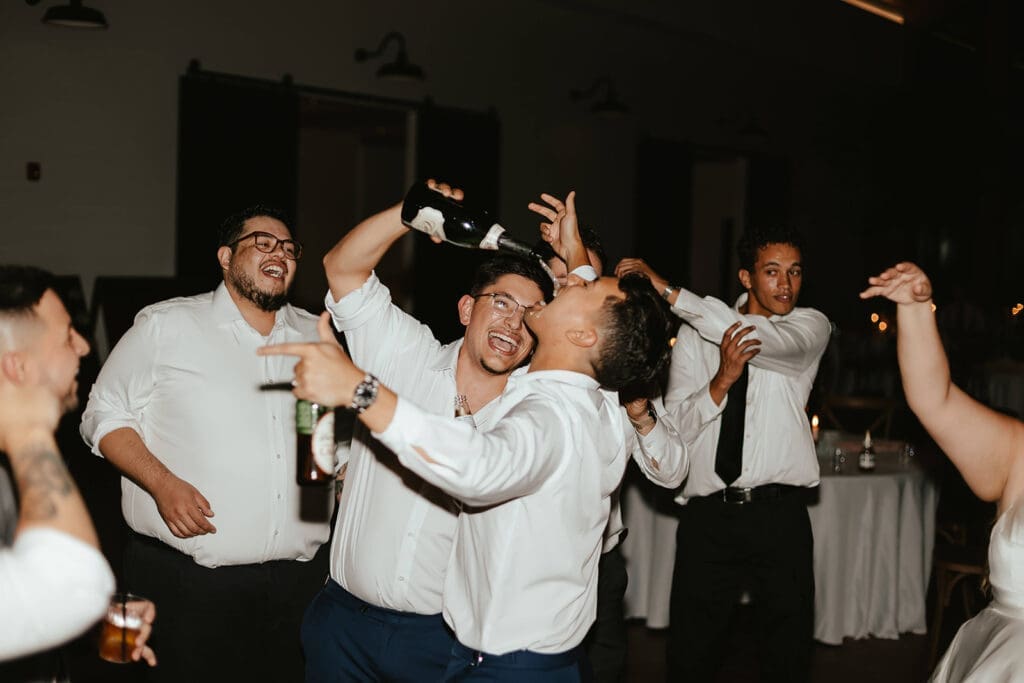 Wedding guest pouring drink into groom's mouth