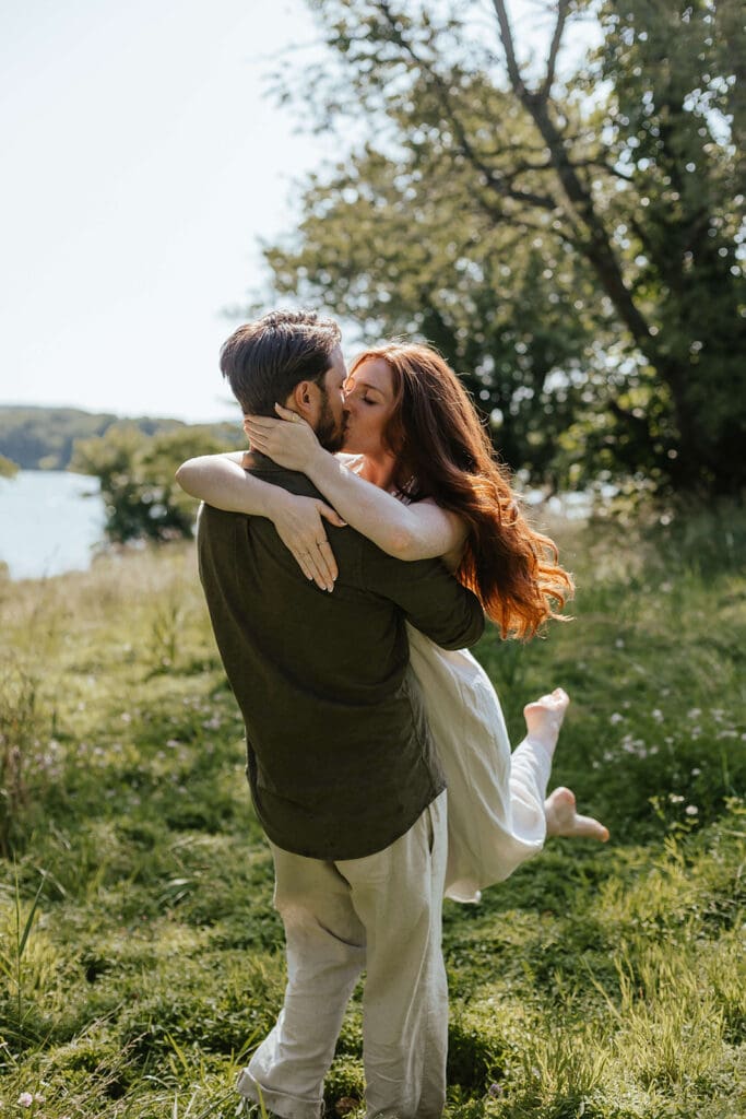 Romantic candid of woman kissing her fiancé during their summer engagement photos in the countryside