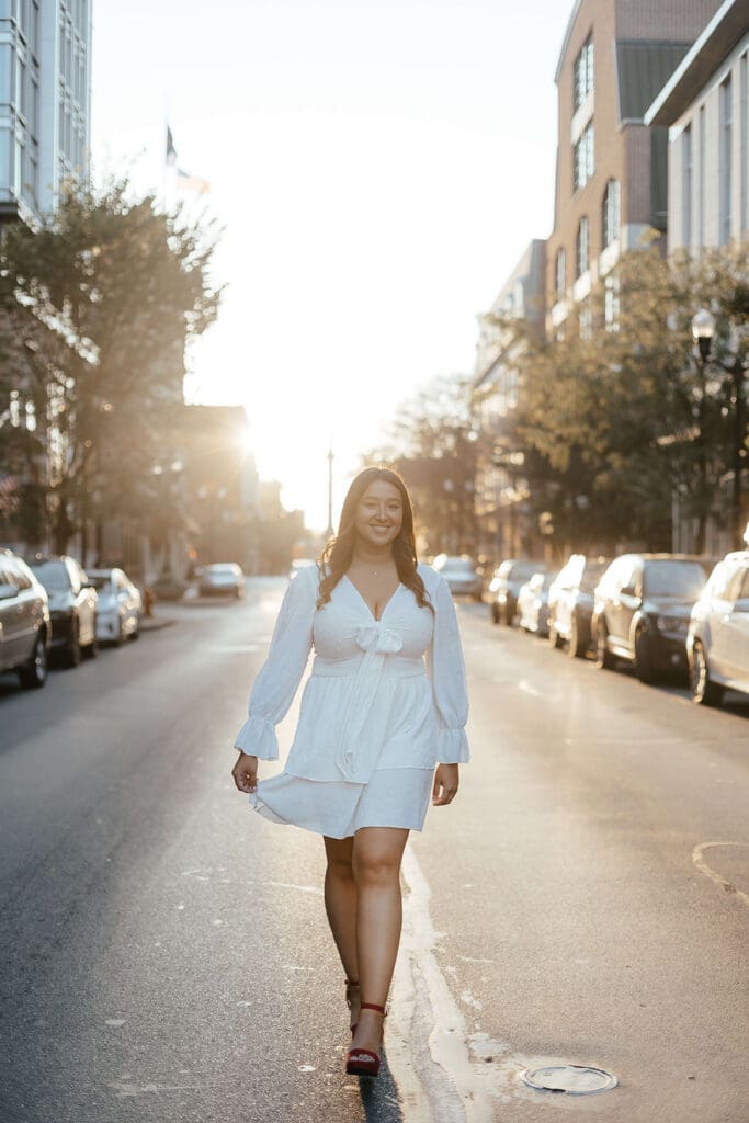 College graduate in white dress walking down the street in Lancaster City during golden hour