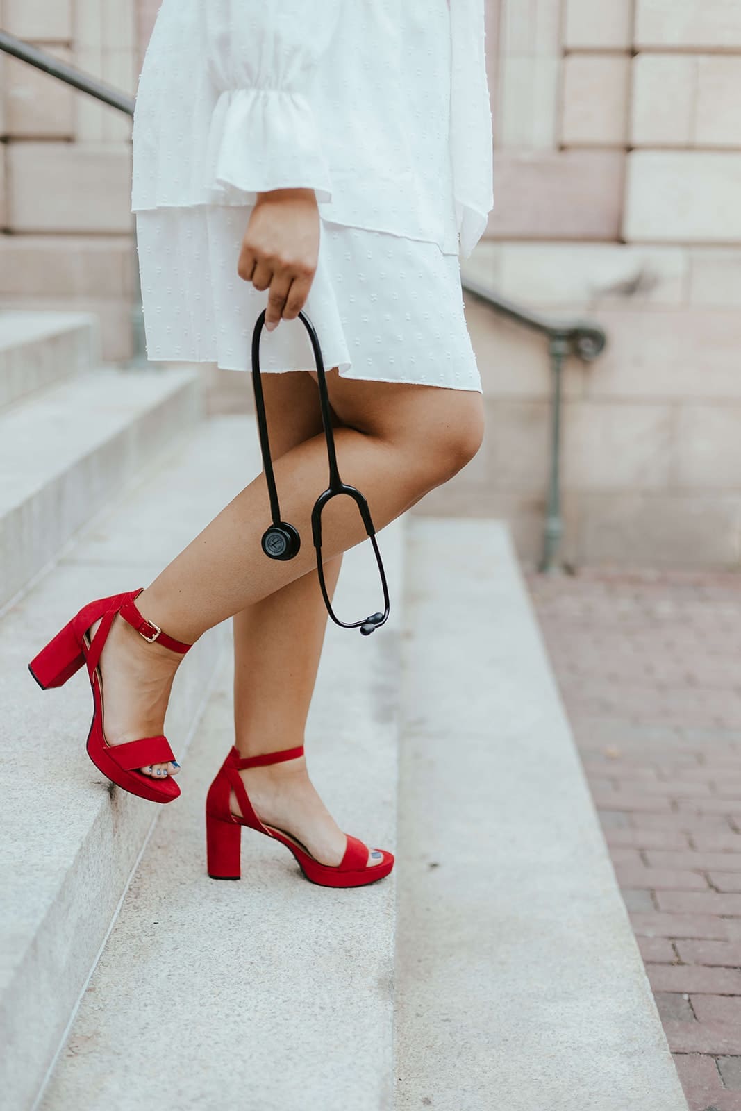 Close up of woman holding stethoscope while walking down the steps of Lancaster County Courthouse in red heels